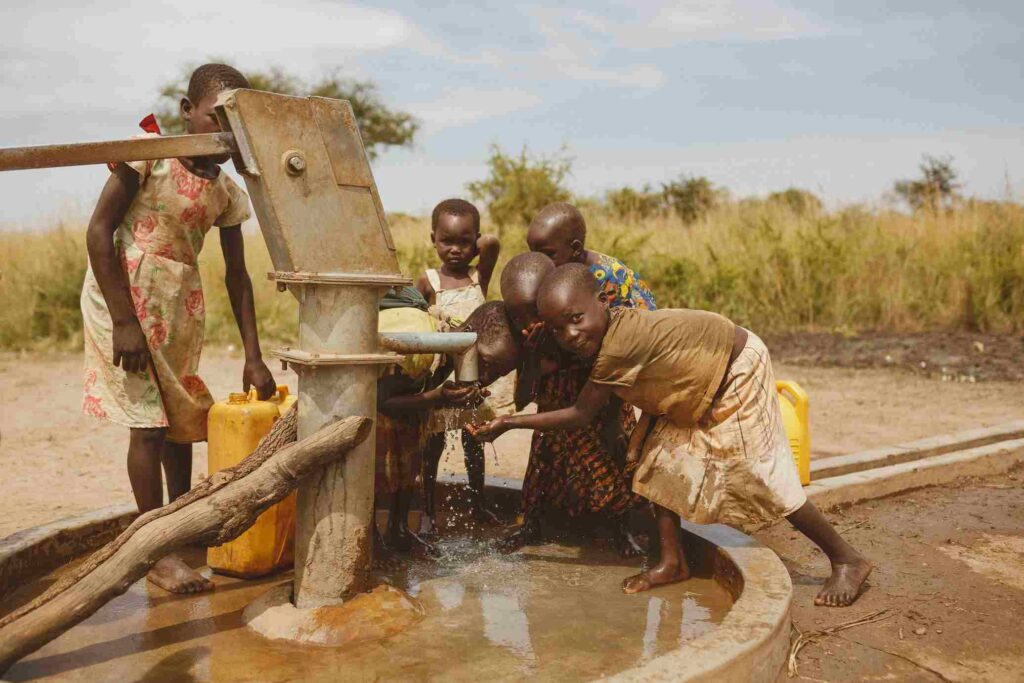 “Children collecting clean drinking water from a community hand pump supported by a non-profit charity organization.”