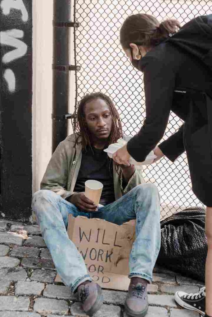 A volunteer offering food to a homeless man sitting on the street as part of a charity outreach program.