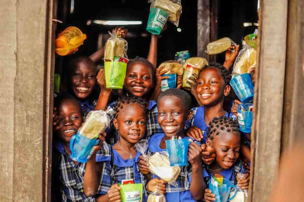 Happy school children holding food and drink packages during a charity food donation program.