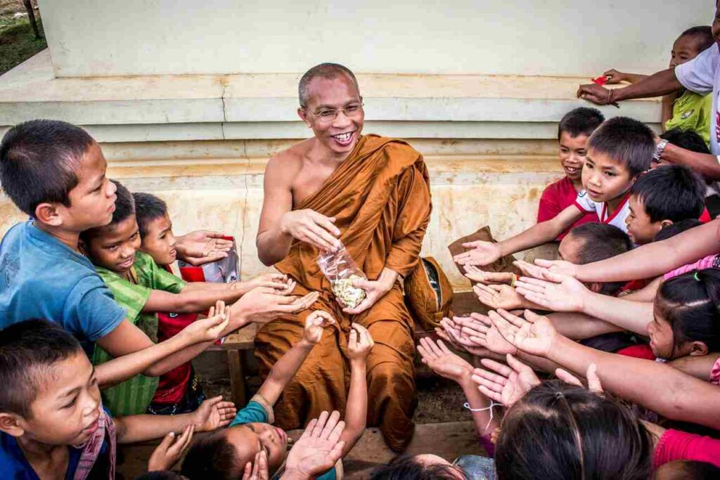 A Buddhist monk sharing food with underprivileged children, showing compassion, charity, and community support.